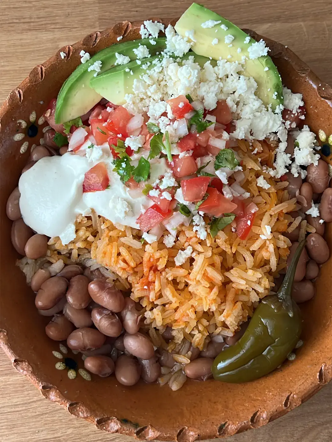 mexican home cooked bowl with pinto beans, rice, avacado, pico de gallo, jalapeno, queso fresco, and sour cream